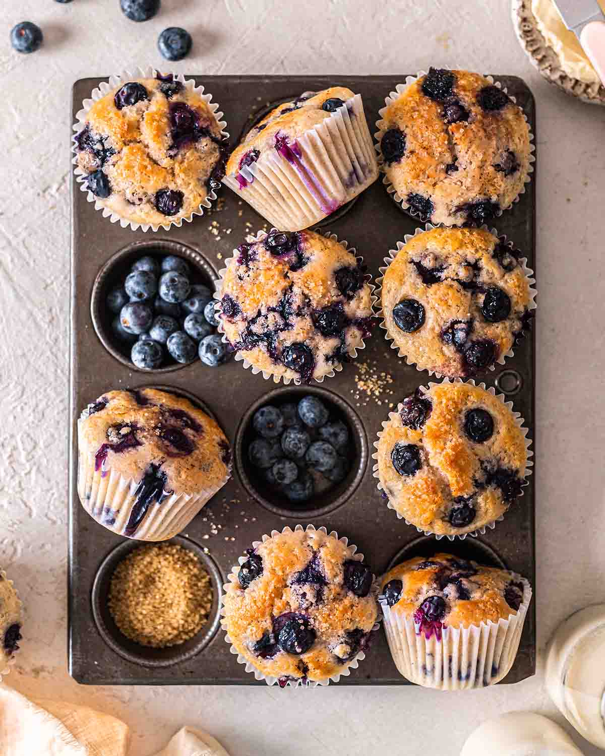 Overhead image of blueberry muffins in tray with pops of purple.