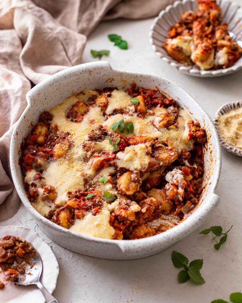 Vegan gnocchi bake with creamy white sauce on top. Portion of gnocchi is removed showing bolognese sauce.