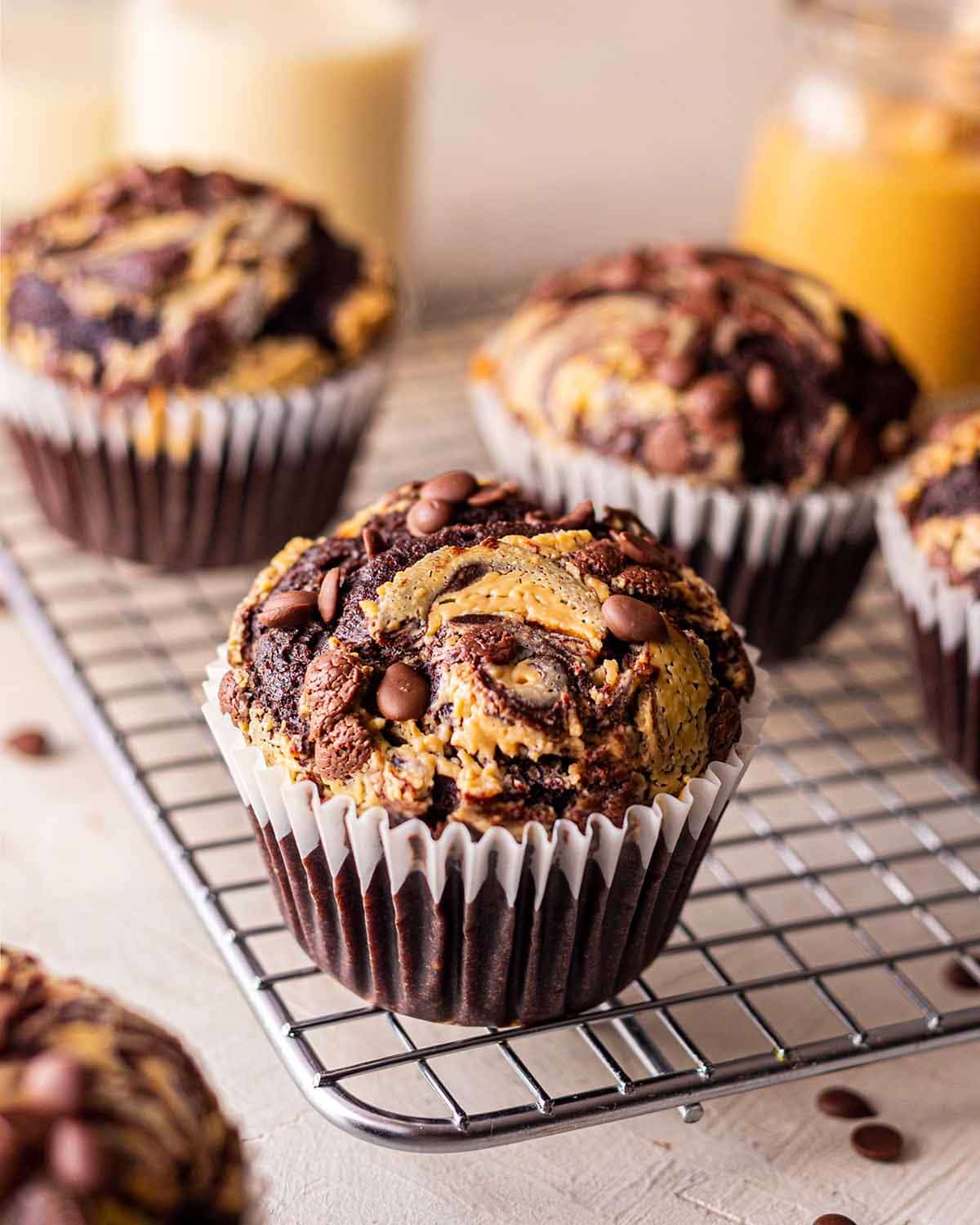 Close up of chocolate peanut butter muffin on wire rack. Muffin has swirl of peanut butter and mini chocolate chips on top.