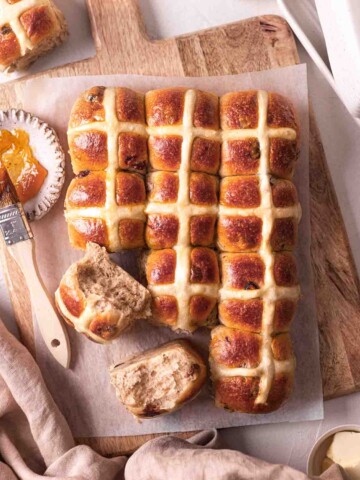 Vegan brioche hot cross buns on chopping board. A few buns are removed showing fluffy texture.