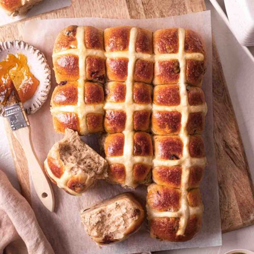 Vegan brioche hot cross buns on chopping board. A few buns are removed showing fluffy texture.