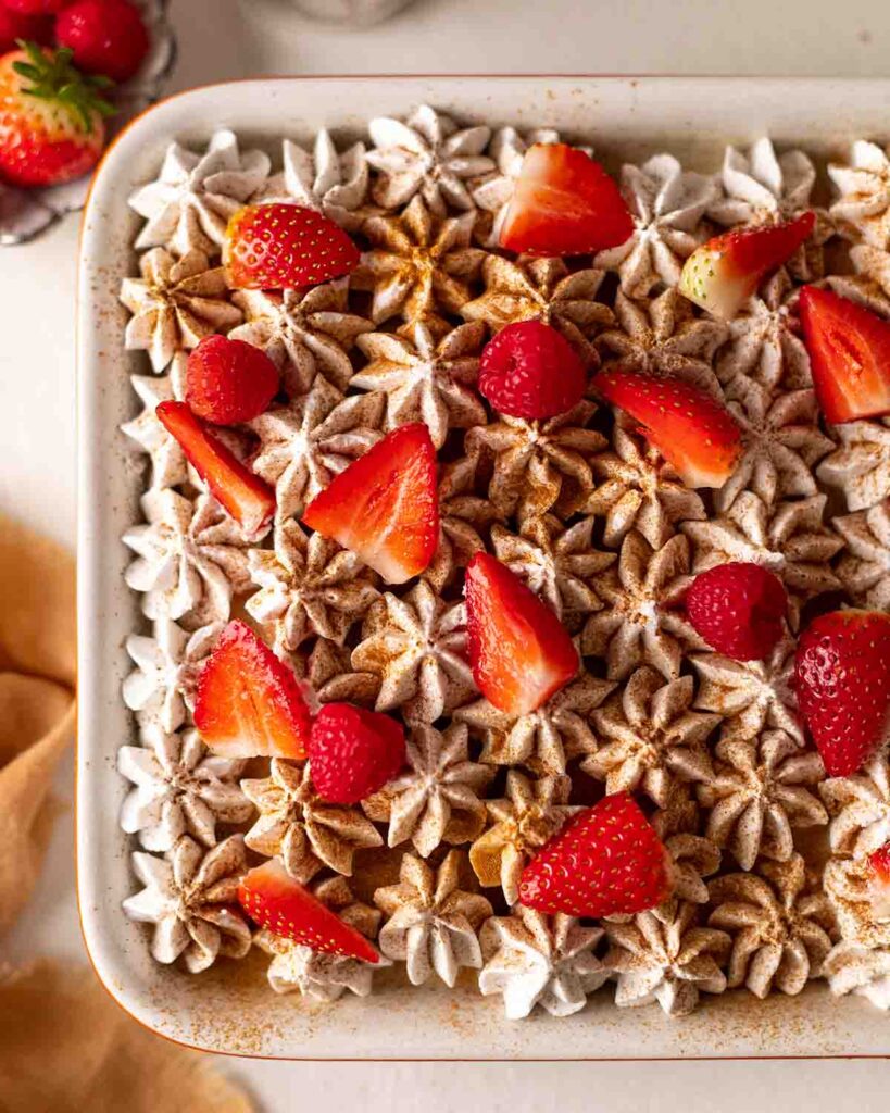 Top of tres leches cake showing piped cream, dusting of ground cinnamon and berries.