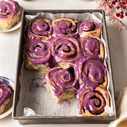 Blueberry rolls with purple cream cheese frosting in baking tray.