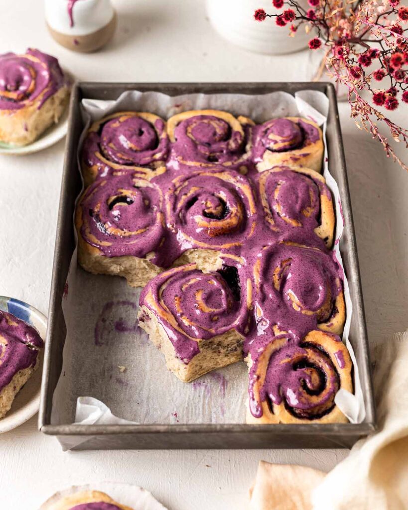 Blueberry rolls with purple cream cheese frosting in baking tray.