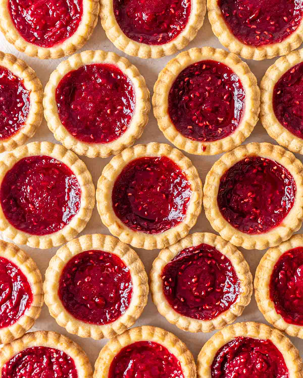 Overhead image of repeated jam tarts emphasising fluted egdes and bright red jam filling.