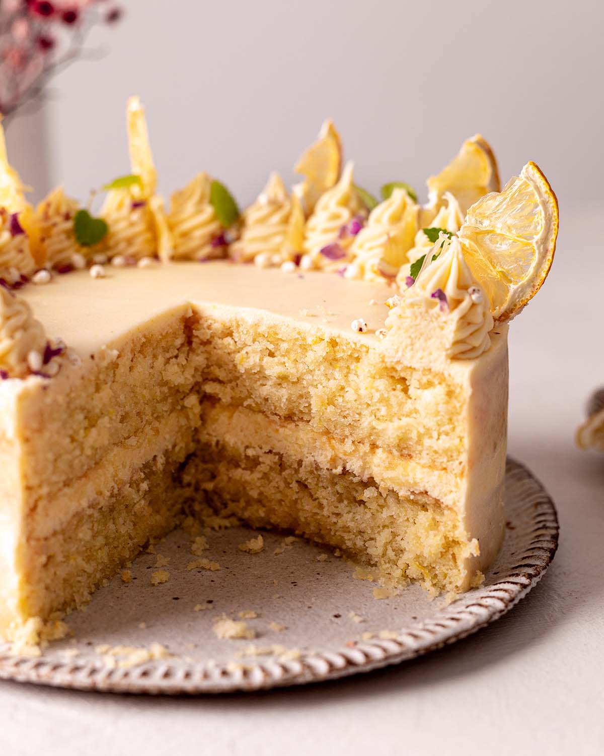 Decorated vegan lemon cake on rustic plate. Cake is cut open showing two etremely fluffy layers of sponge cake.