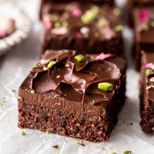 Close up of no-bake brownies on parchment paper showing fudgy texture and smooth frosting.