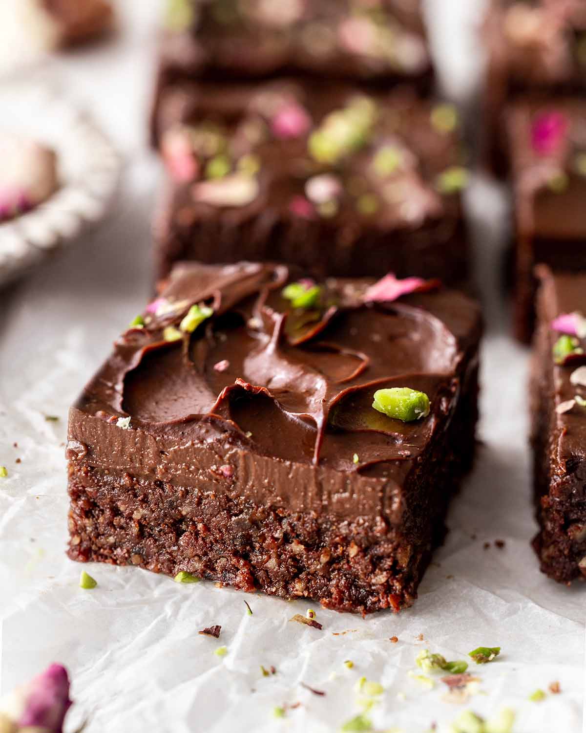 Close up of no-bake brownies on parchment paper showing fudgy texture and smooth frosting.