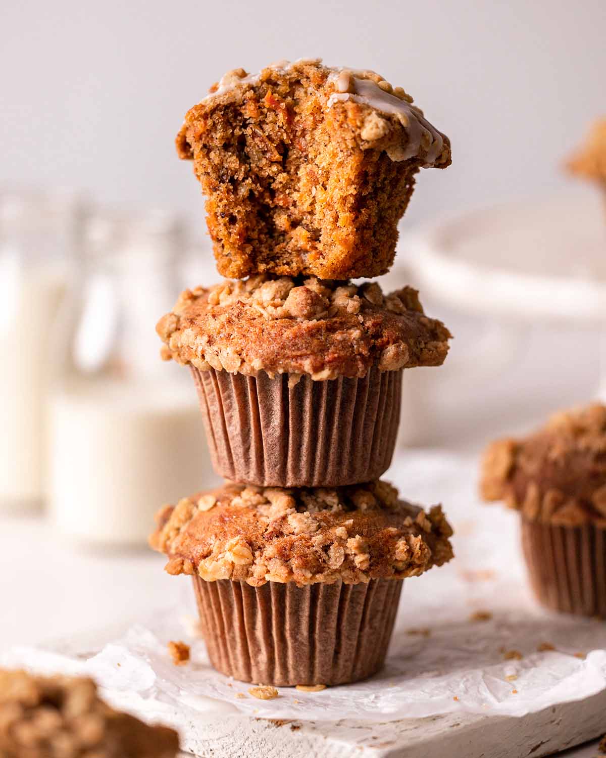 Stack of vegan carrot muffins. One muffin has been bitten showing fluffy orange texture.