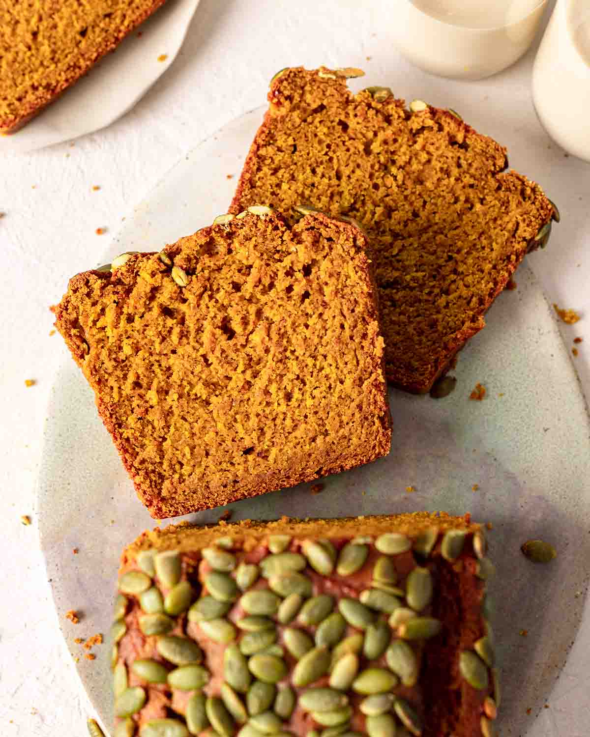 Vegan pumpkin bread on platter with two slices cut out showing fluffy golden texture.