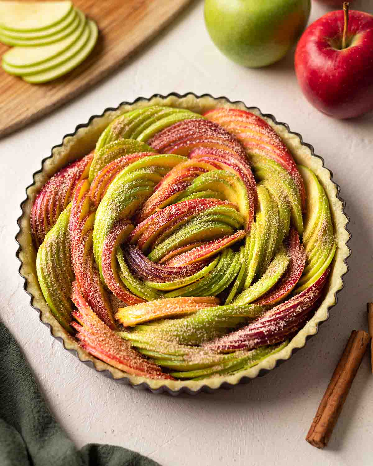 Unbaked vegan apple tart filled with thinly sliced red and green apples.