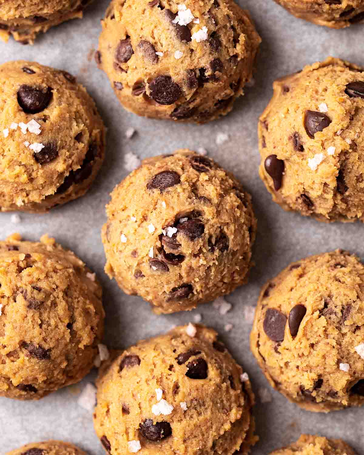 Close up of small ice cream scoops of cookie dough with sprinkle of flaked salt on parchment paper.