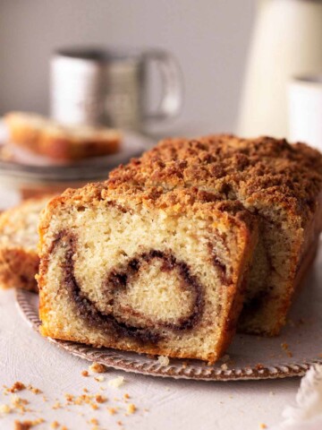 Vegan cinnamon bread loaf on rustic plate with a few slices cut out with focus on dark cinnamon swirl.