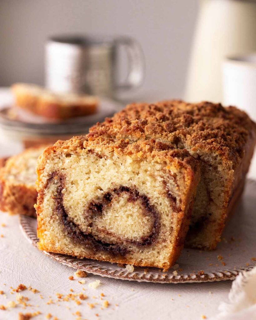 Vegan cinnamon bread loaf on rustic plate with a few slices cut out with focus on dark cinnamon swirl.