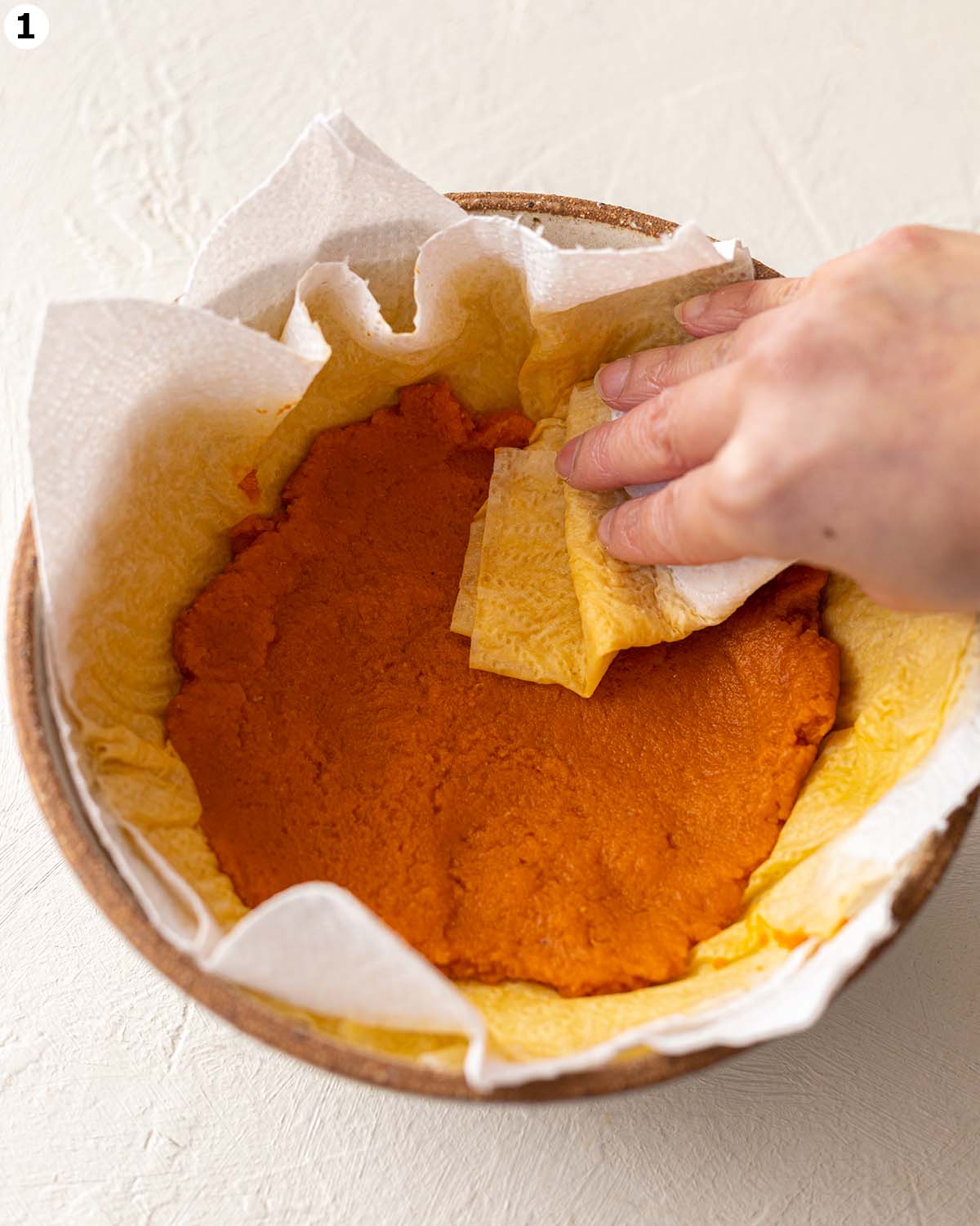 Pumpkin puree on paper towels in bowl. Hand is blotting pumpkin with another paper towel.