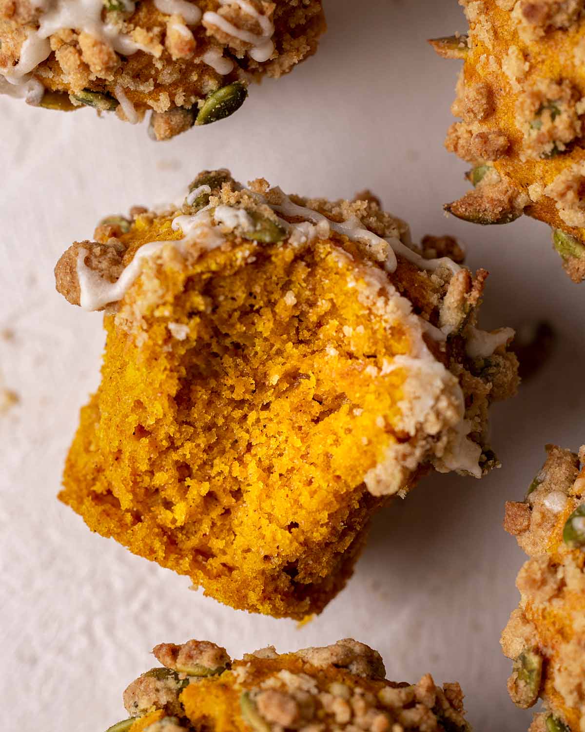 Close up of one muffin with bite taken out showing fluffy texture and orange color from the pumpkin.