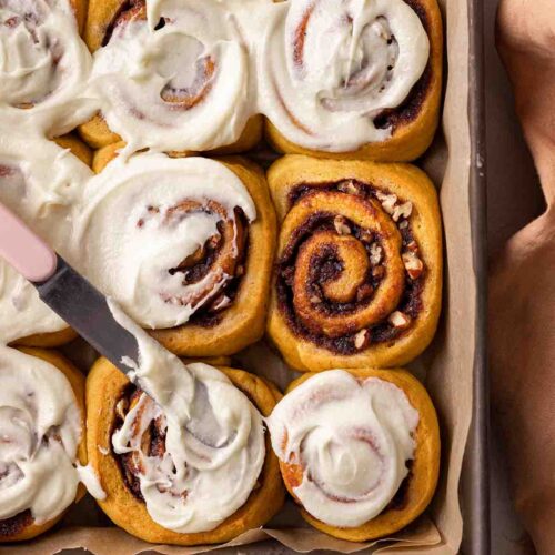 Close up of gold-colored pumpkin cinnamon rolls in with one roll without frosting.