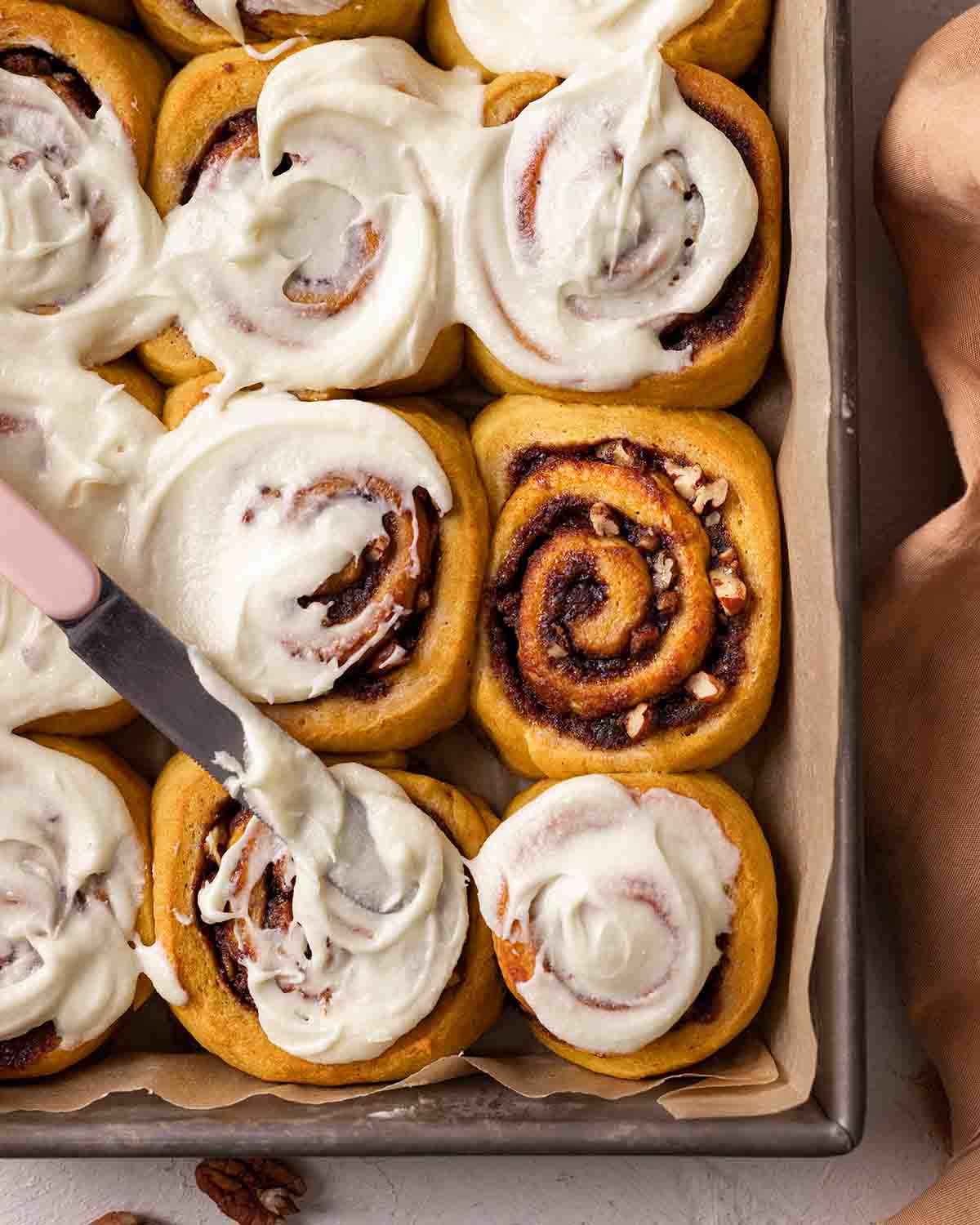 Close up of gold-colored pumpkin cinnamon rolls in with one roll without frosting.