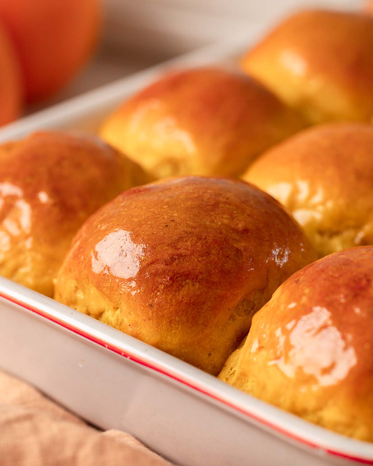 Close up of one tall and golden dinner roll amongst the other rolls in baking tray.