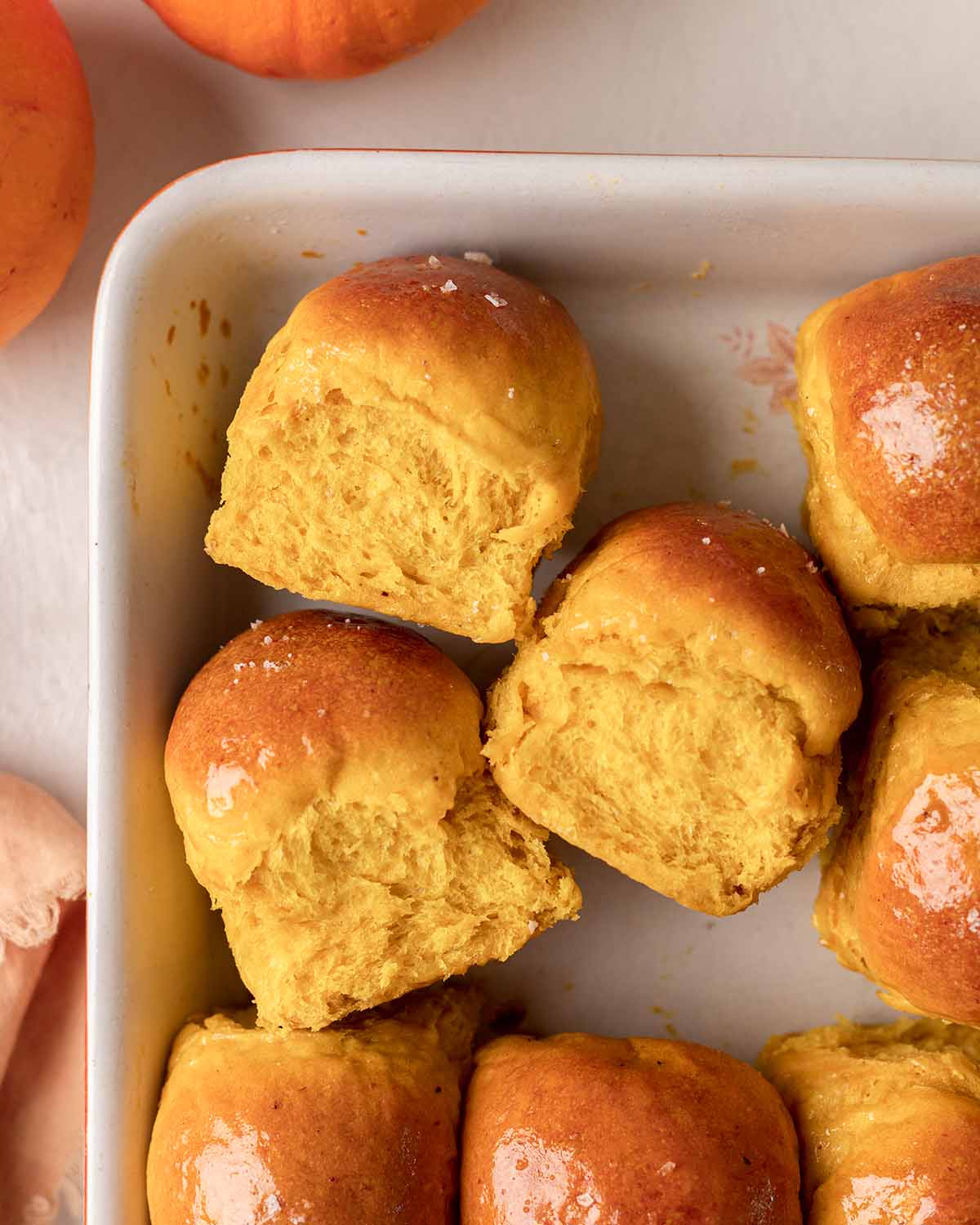 Baking tray filled with pumpkin rolls with a few on their side showing fluffy texture.