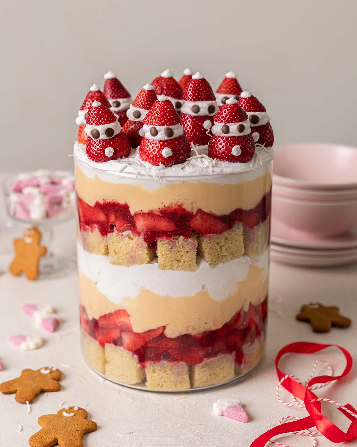 Trifle with layers of cubed cake, jammy strawberries, creamy custard and cream, topped with strawberries decorated as mini Santas.