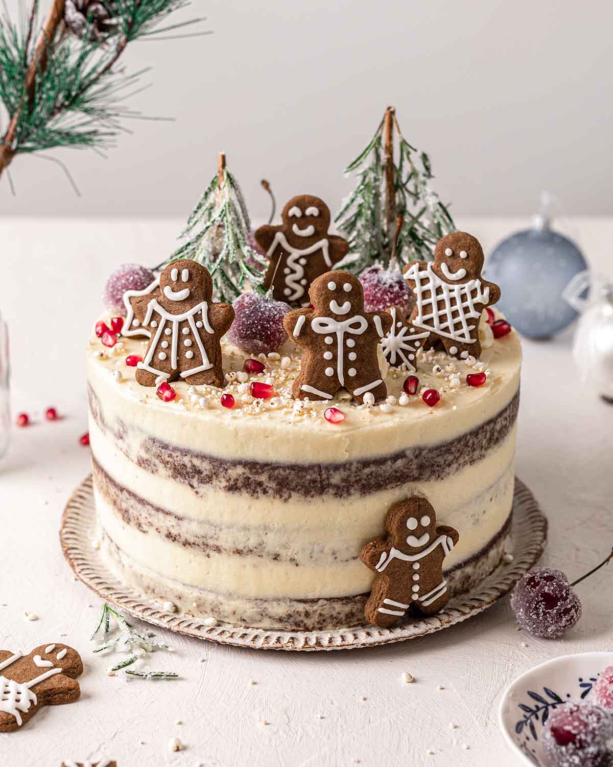 Fully decorated gingerbread cake with thin layer of frosting, topped with cookies, sugared cherries and rosemary.