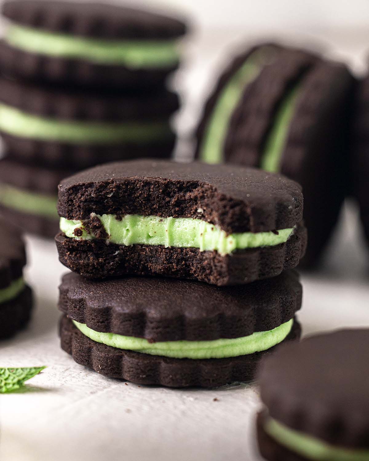 Close up of two cookies. One cookie has bite taken out showing crunchy texture and smooth green mint cream filling.