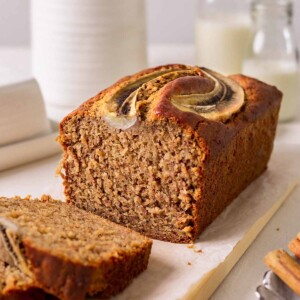 Vegan banana bread on wooden serving board with two slices cut off revealing fluffy golden texture.