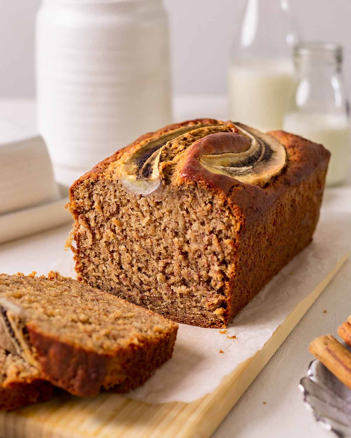 Vegan banana bread on wooden serving board with two slices cut off revealing fluffy golden texture.