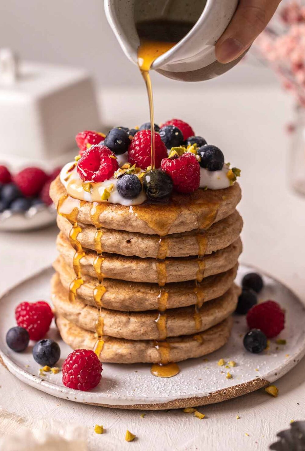 Tall stack of decorated whole wheat pancakes with maple syrup poured on top and dripping down sides.