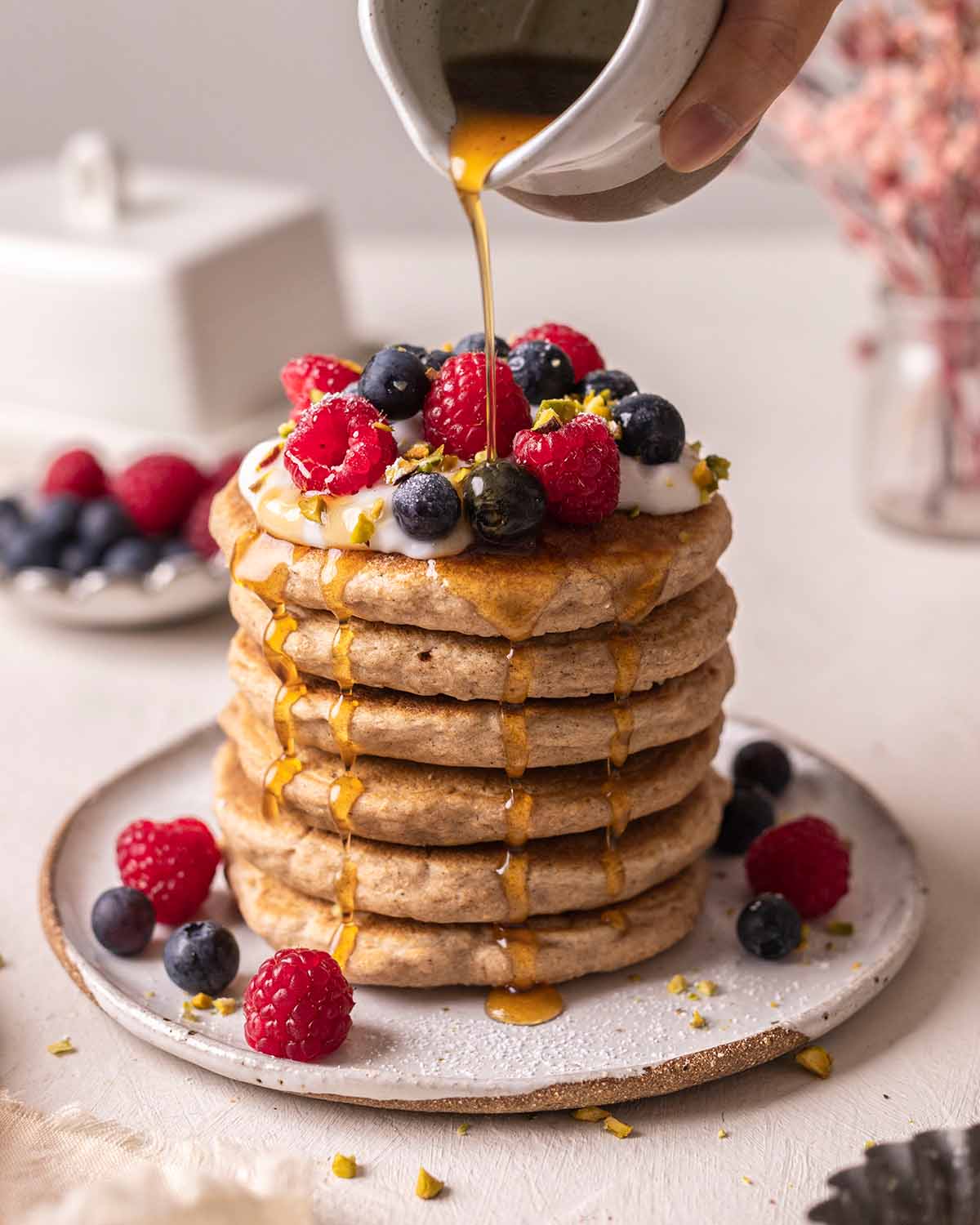 Tall stack of decorated whole wheat pancakes with maple syrup poured on top and dripping down sides.