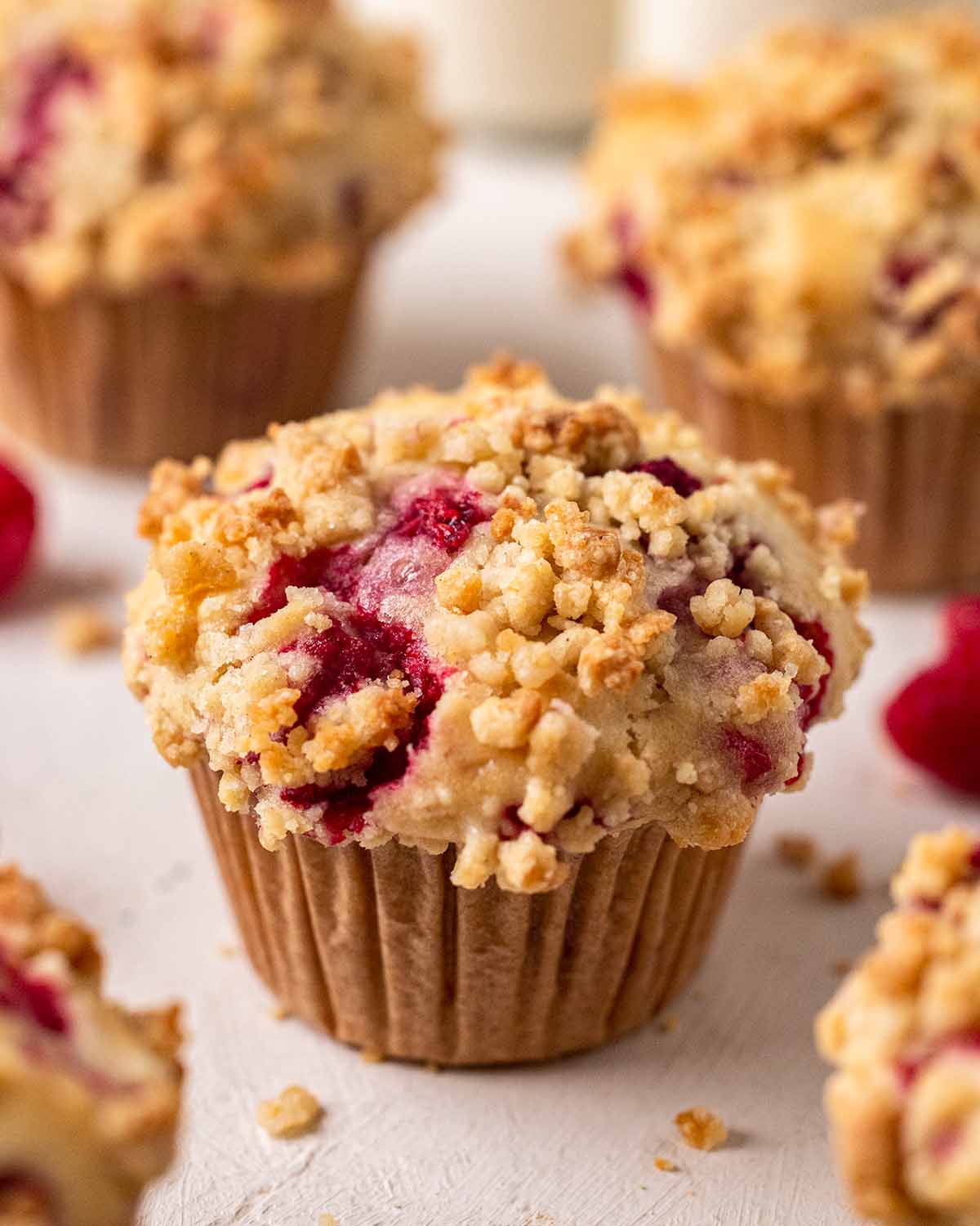 Close up of vegan raspberry muffin with a tall muffin top. The muffin has a golden crumble and raspberry showing through.