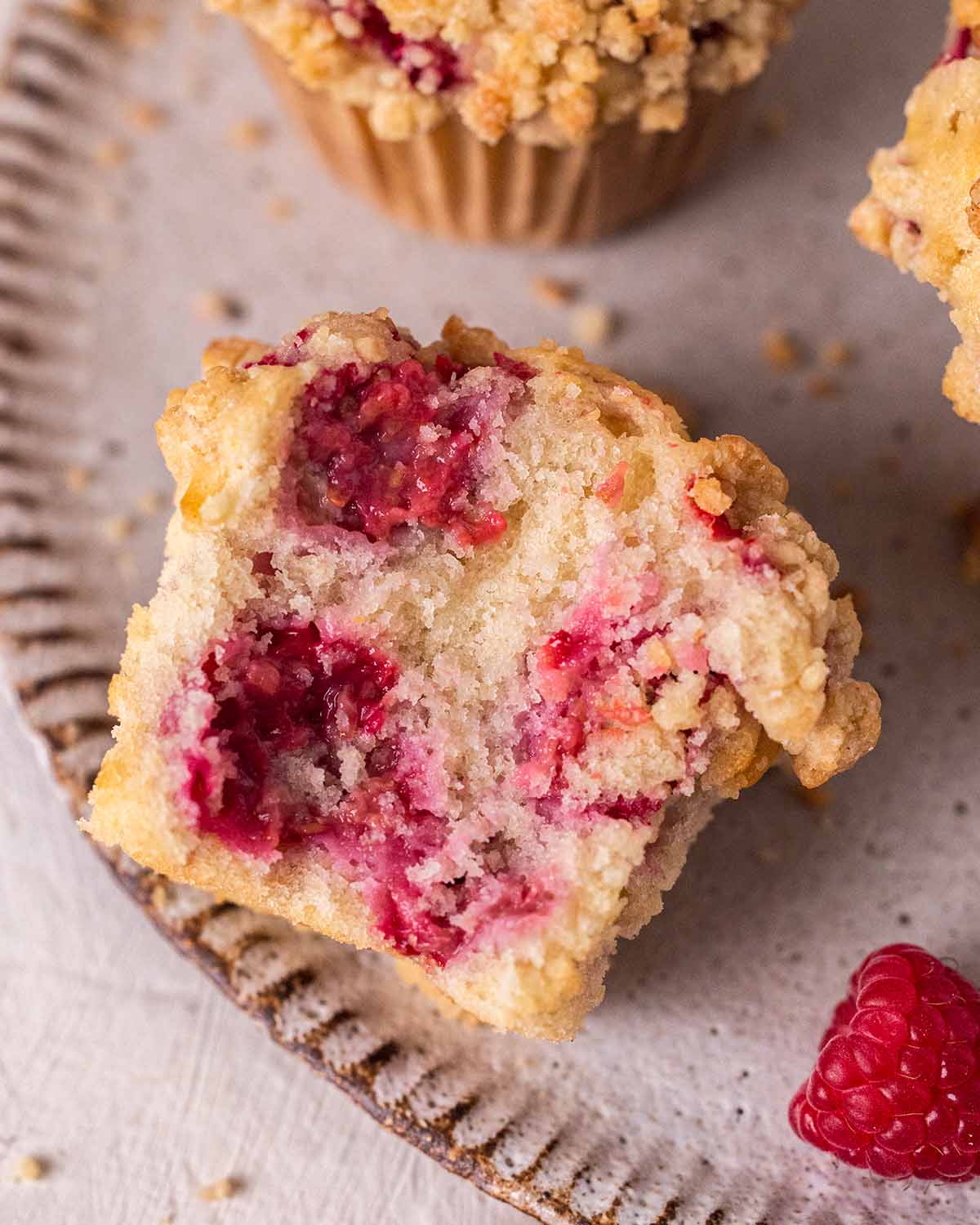 Close up of one muffin with bite taken out showing fluffy texture and juicy raspberries.