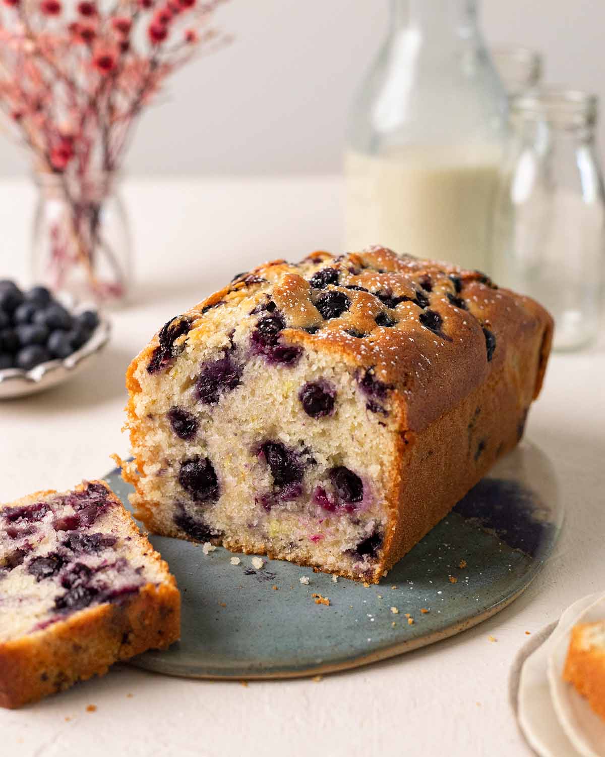 Vegan blueberry bread on plate with slice cut off showing fluffy texture.