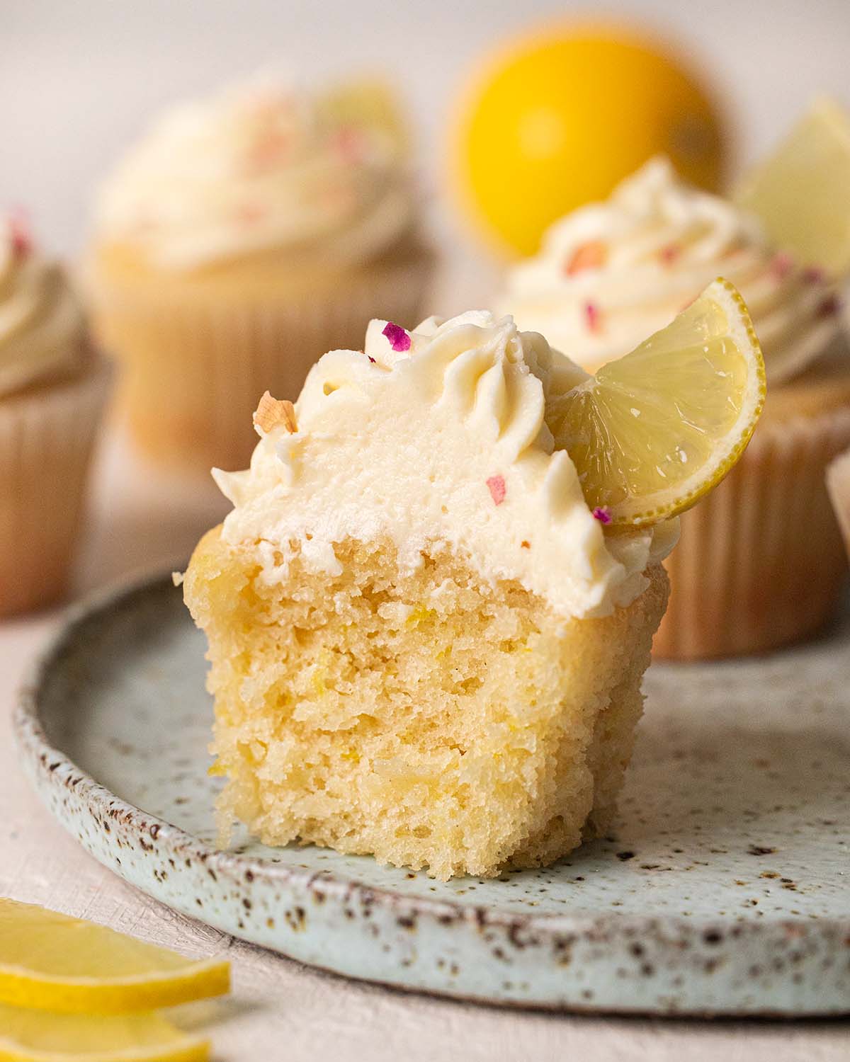 Close up of lemon cupcake with bite taken out showing texture of cupcake and frosting.
