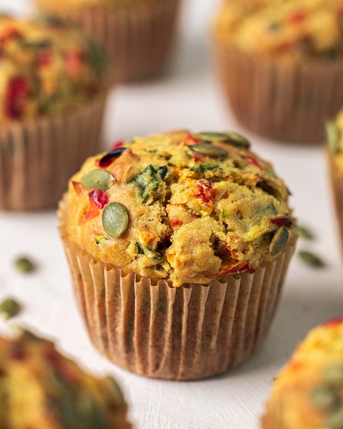 Close up of vegan savoury muffin showing tall muffin top with vegetables showing through the surface.