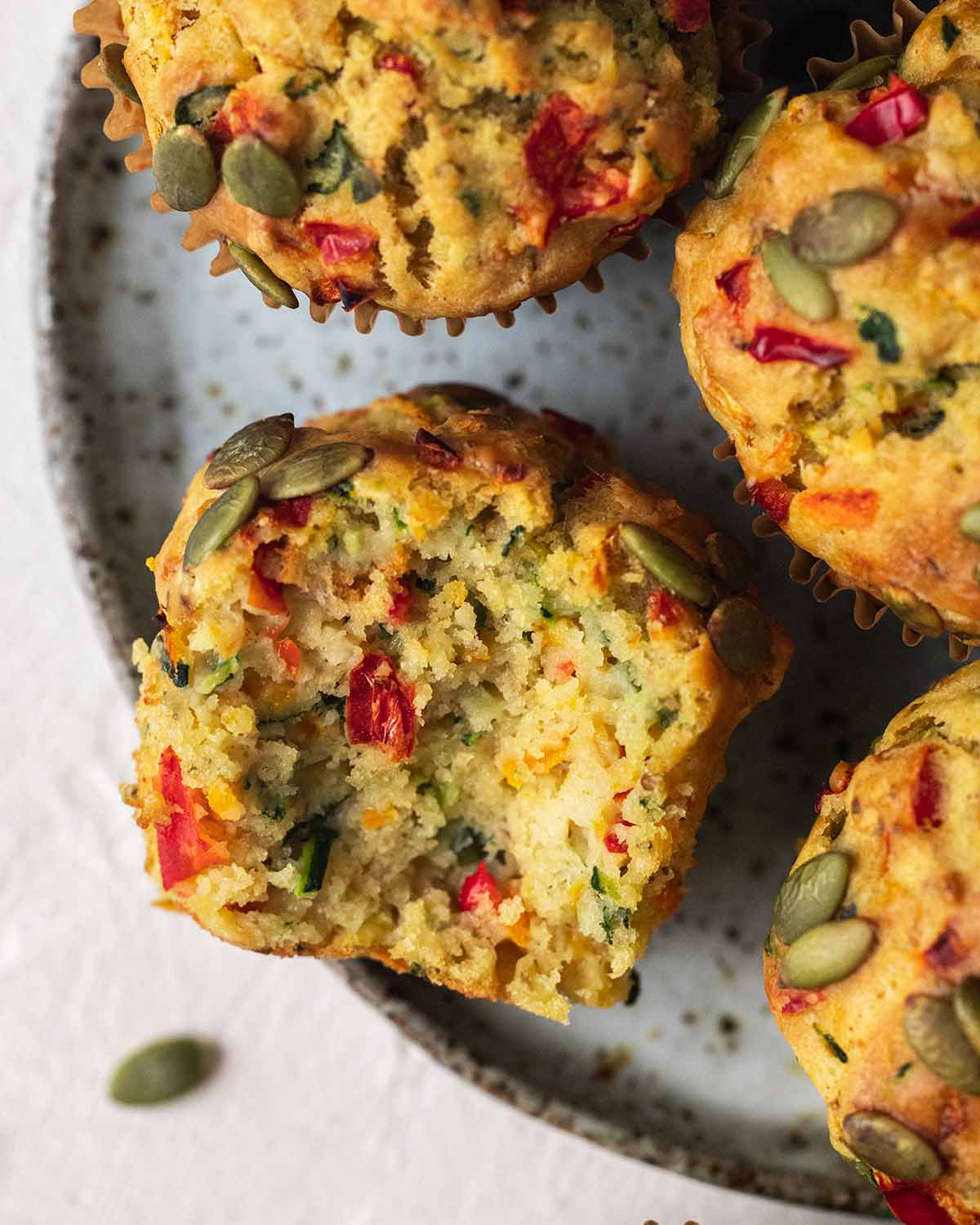 Close up of savoury muffins on plate with one muffin on its side with bite taken, showing fluffy texture.