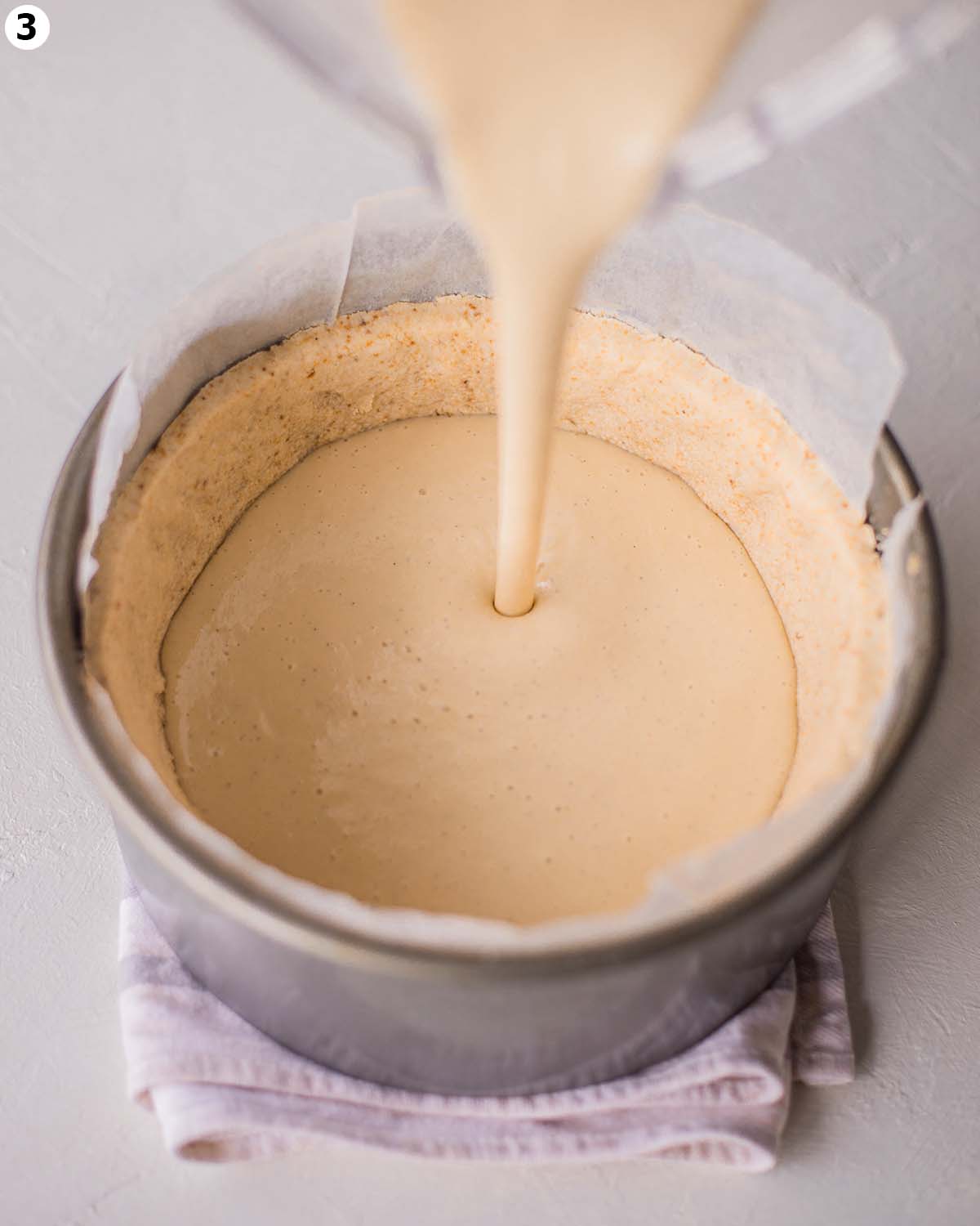 Blender pouring smooth cheesecake mixture into par-baked crust.