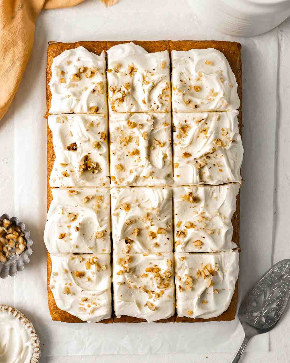Overhead image of banana cake with cream cheese frosting and chopped walnuts, cut into serves.