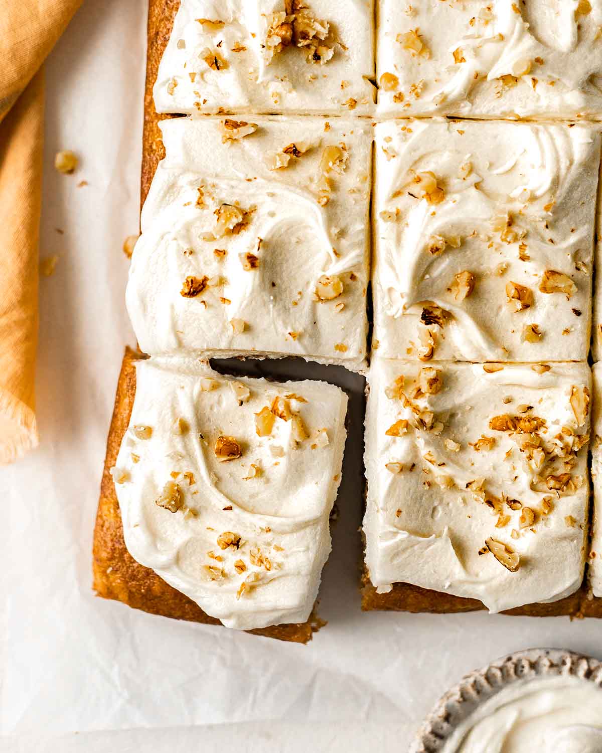 Overhead image of banana cake with cream cheese frosting and chopped walnuts, cut into serves.