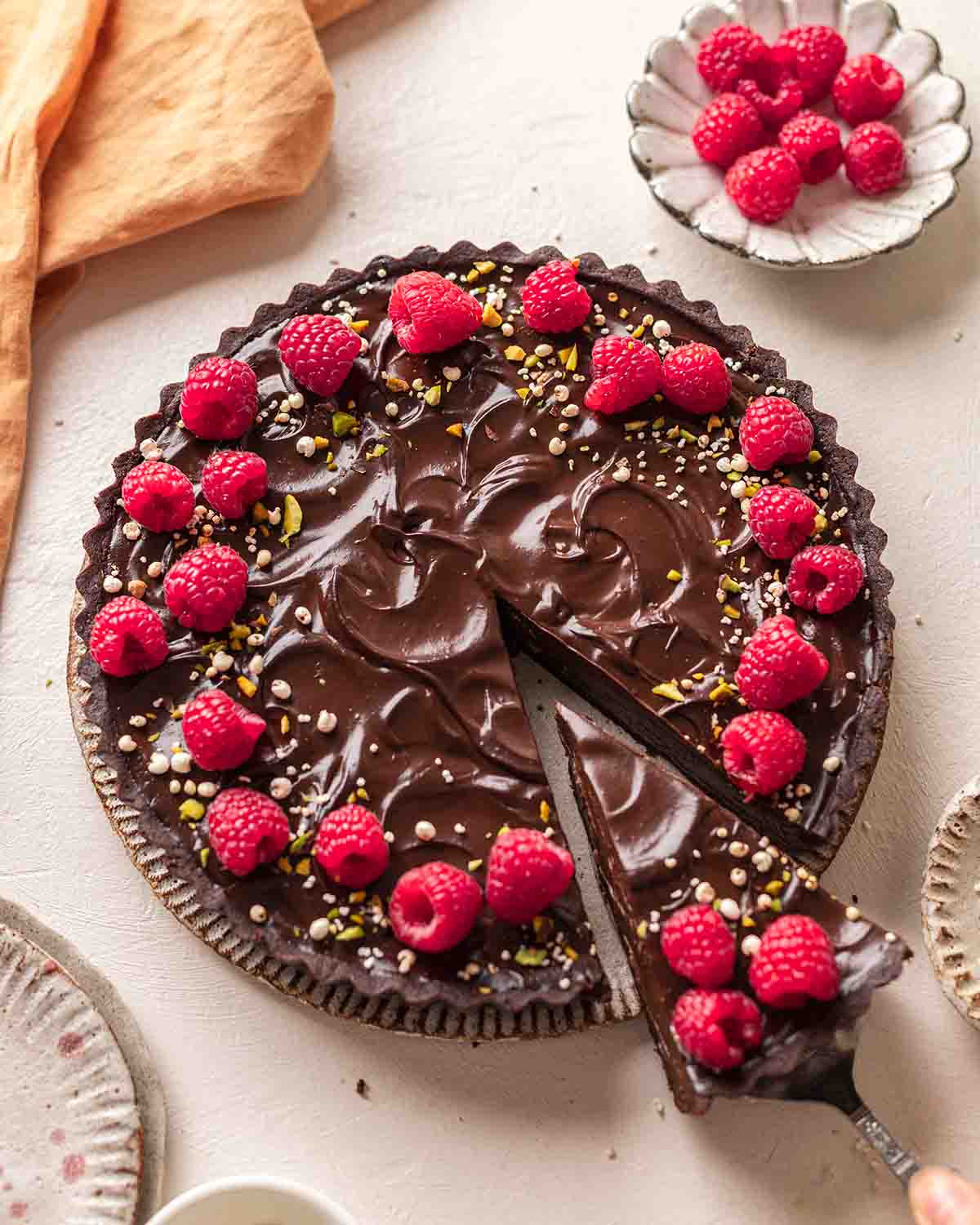 Avocado tart on plate with very glossy surface and raspberries on top.