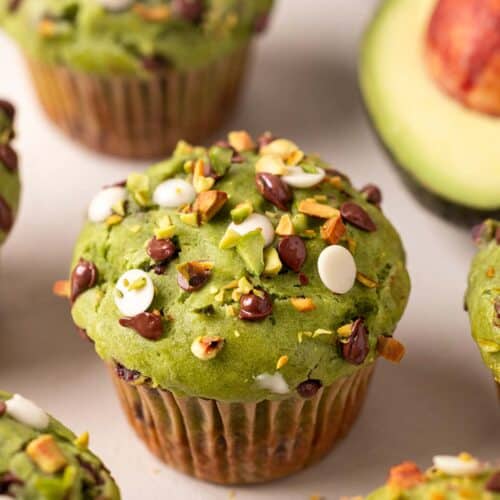 Close up of avocado muffin focusing on top which has dark and white chocolate chips and chopped pistachios.