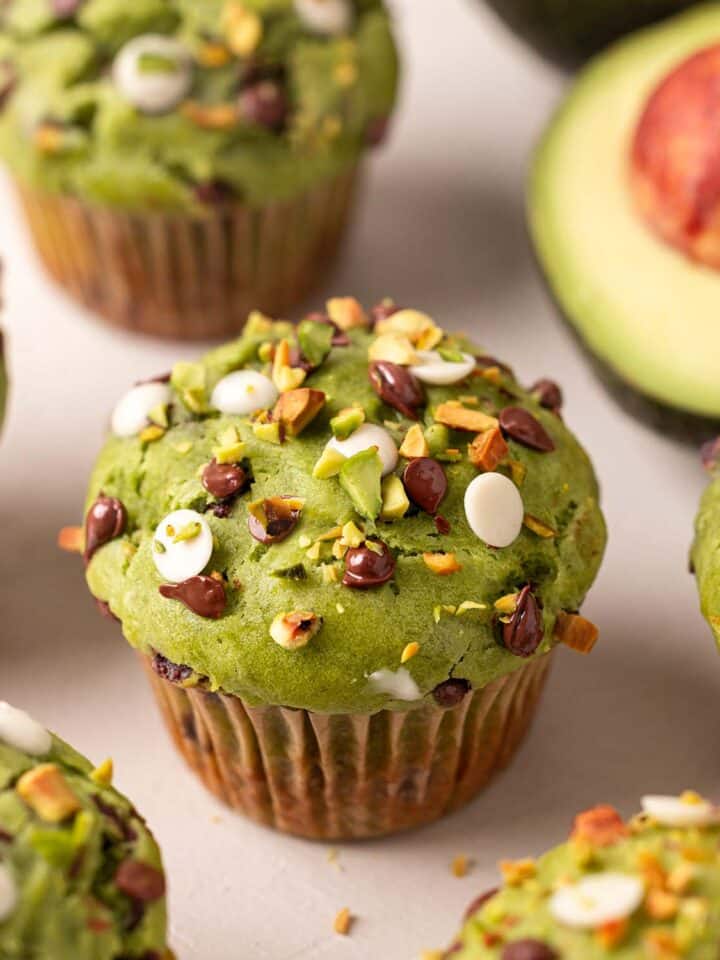 Close up of avocado muffin focusing on top which has dark and white chocolate chips and chopped pistachios.