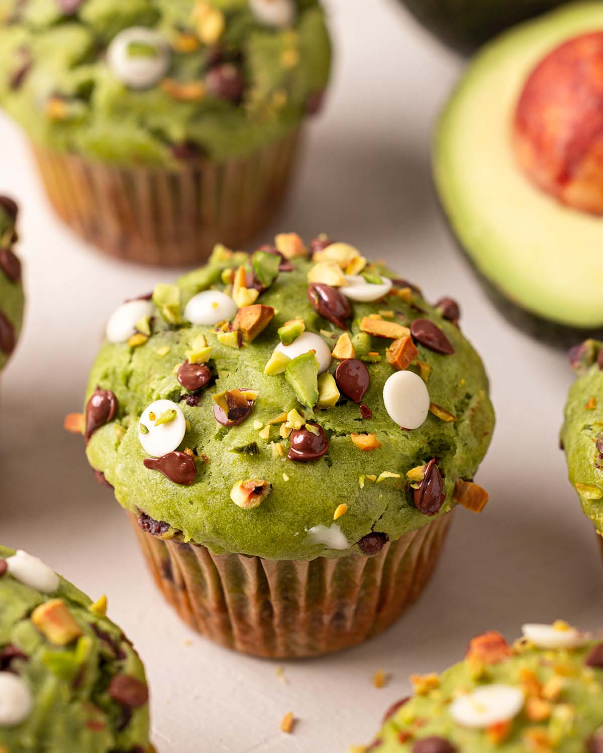 Close up of avocado muffin focusing on top which has dark and white chocolate chips and chopped pistachios.