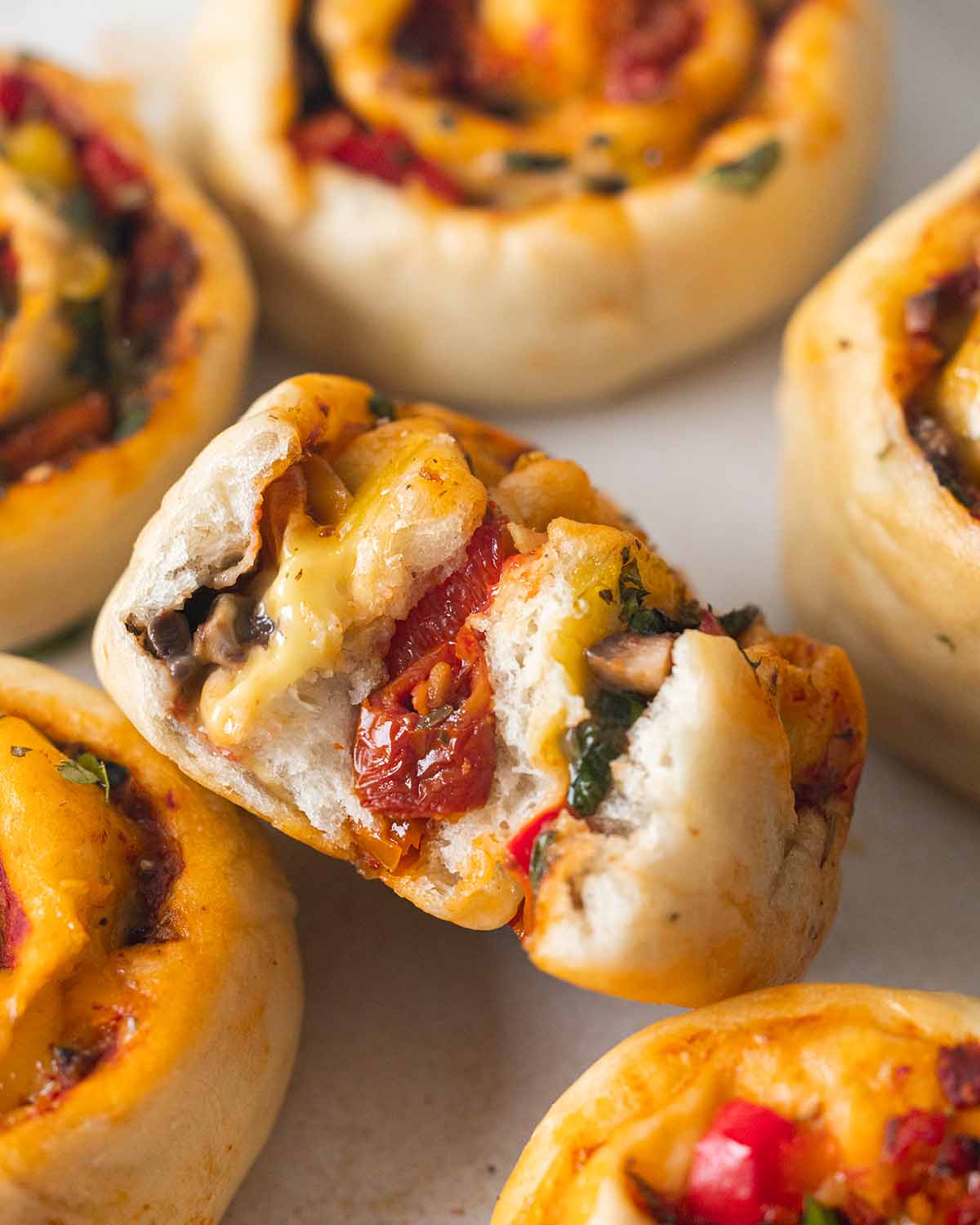 Close up of cross section of a pizza roll showing the crust's fluffy texture and layers of vegan cheese and vegetables.