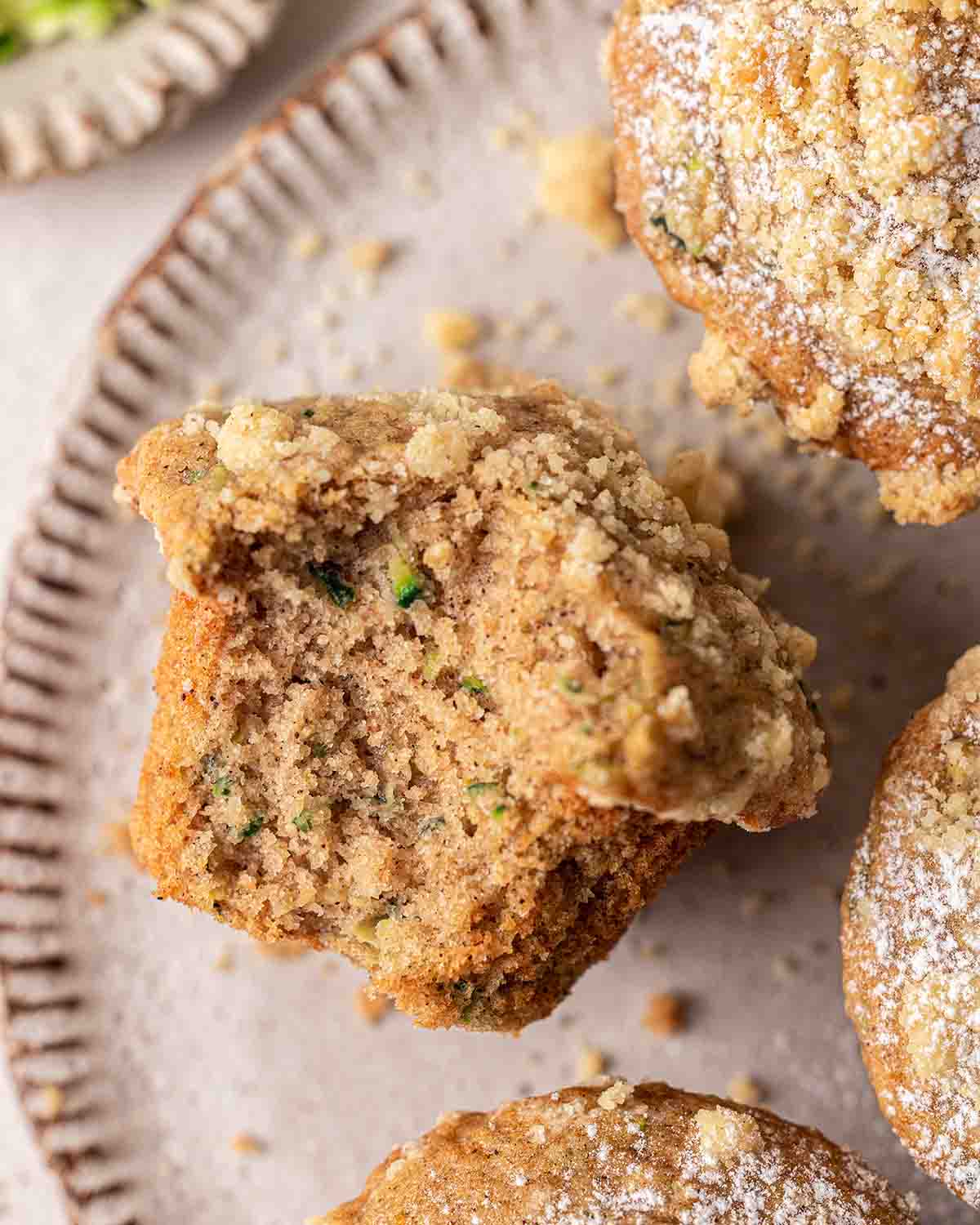 Close up of zucchini muffin with bite taken out showing fluffy texture and specks of zucchini.