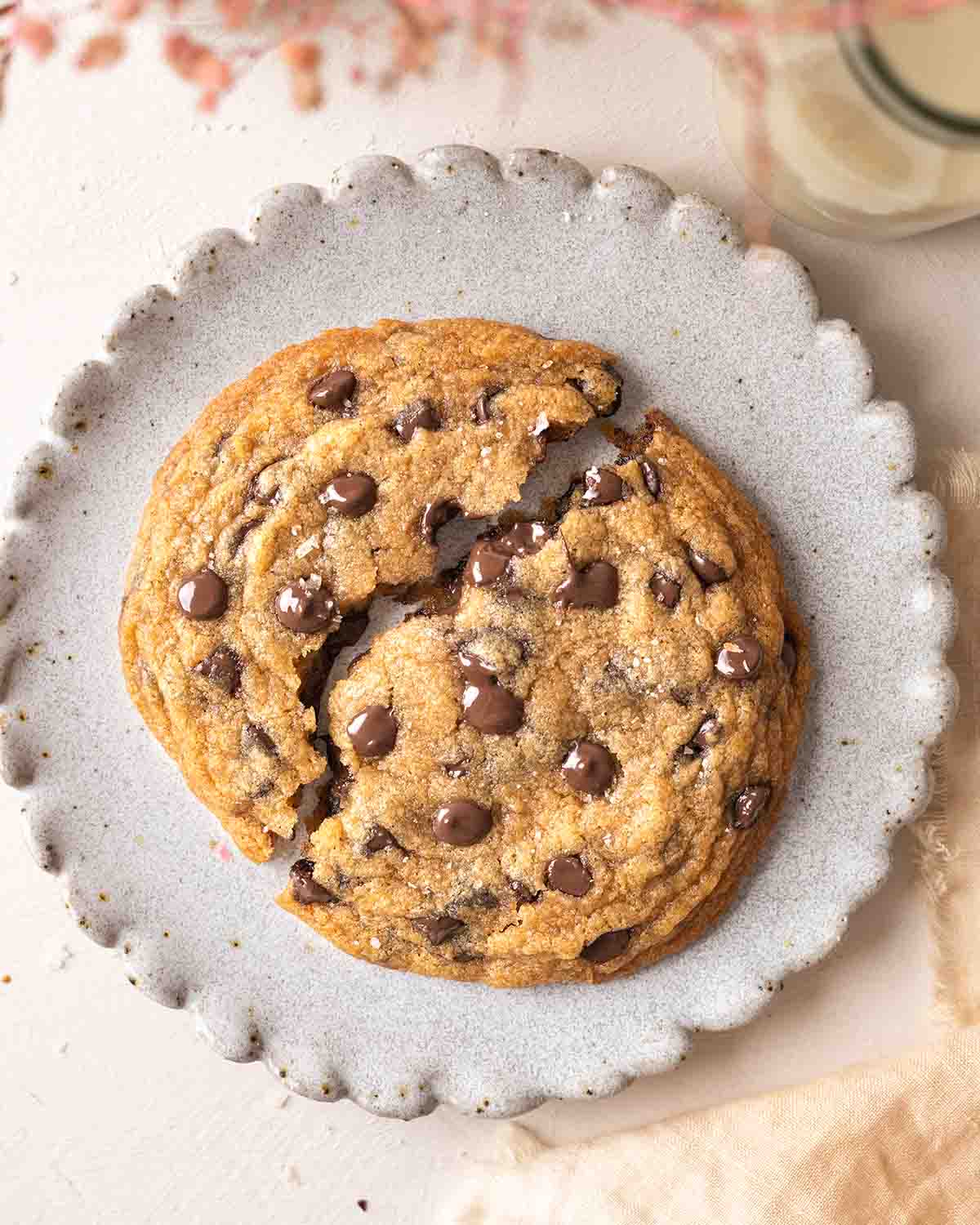 Large vegan cookie on plate broken in half with melty chocolate chips.