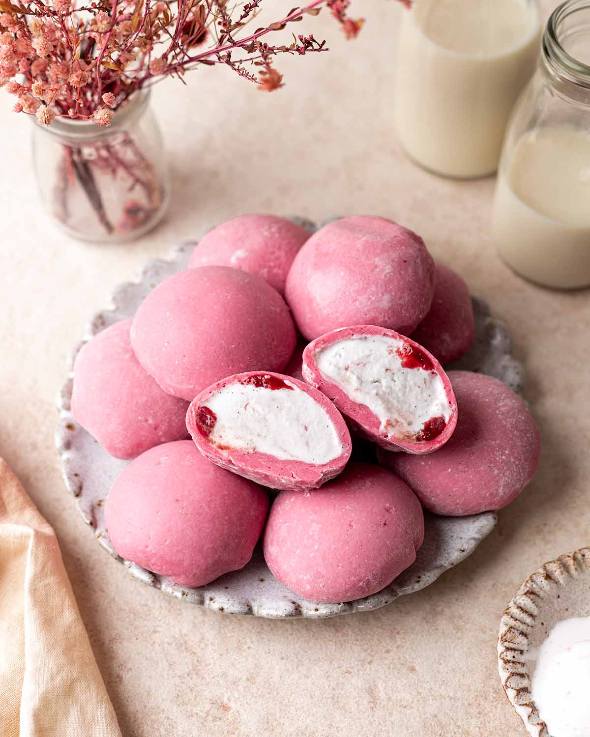 Balls of pink-colored strawberry mochi ice cream on plate with one mochi cut open revealing vanilla ice cream and strawberry jam filling