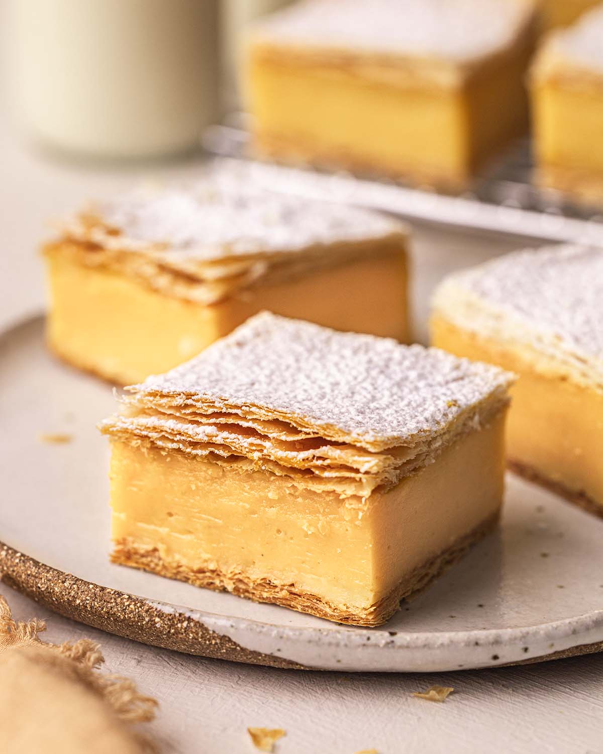 Close up of vanilla slice on a plate. The slice has two flaky layers of puff pastry sandwiching a thick layer of custard.