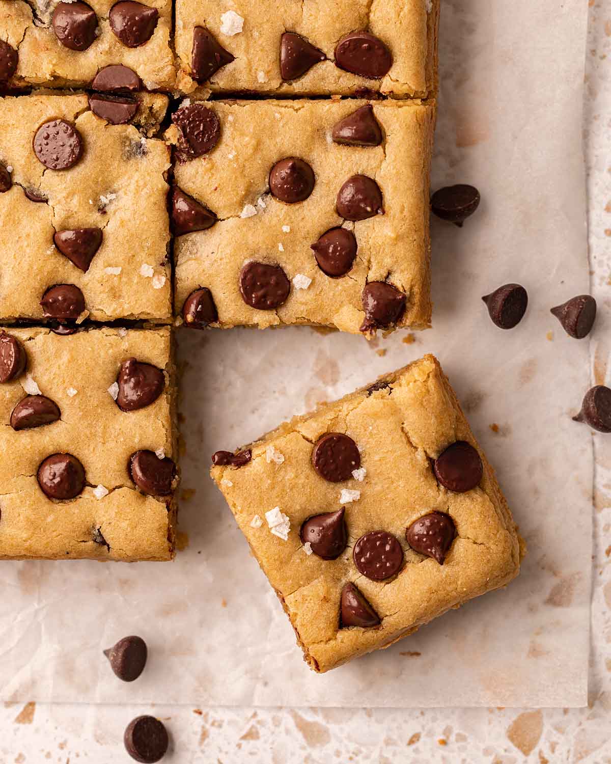 Overhead image of blondies on parchment paper with one blondie bar removed.